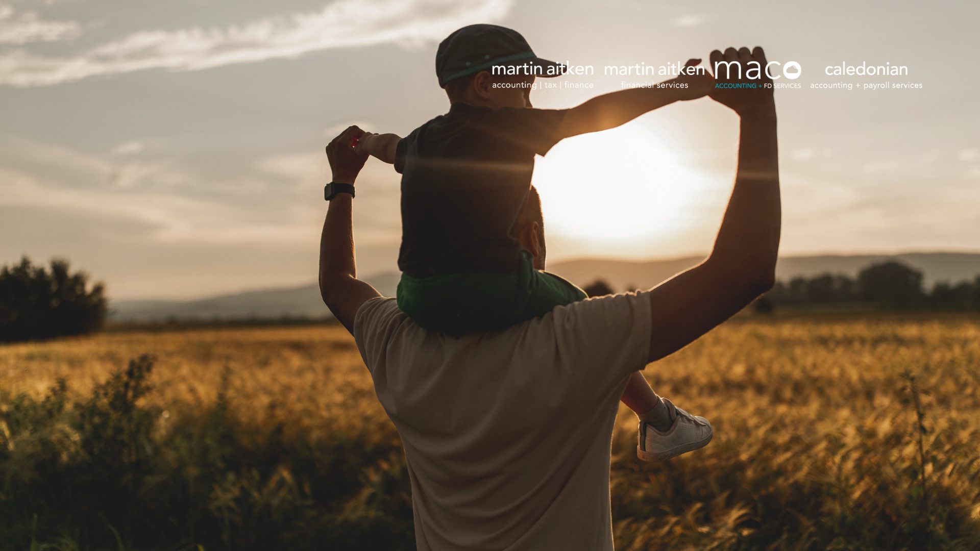 Man with child sitting on shoulders watching the sunset in a a hay field